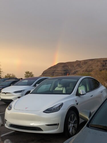 Melody the white Tesla Model Y with a rainbow over the mountains in the background